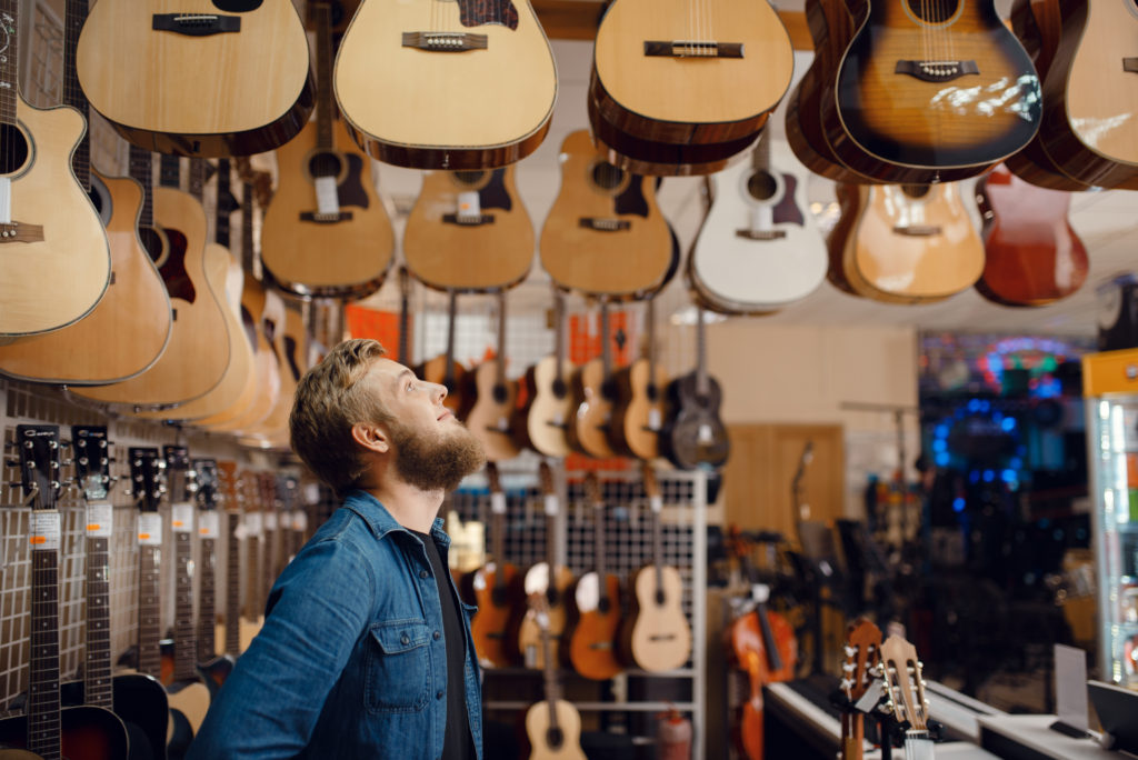 Young guy choosing acoustic guitar in music store
